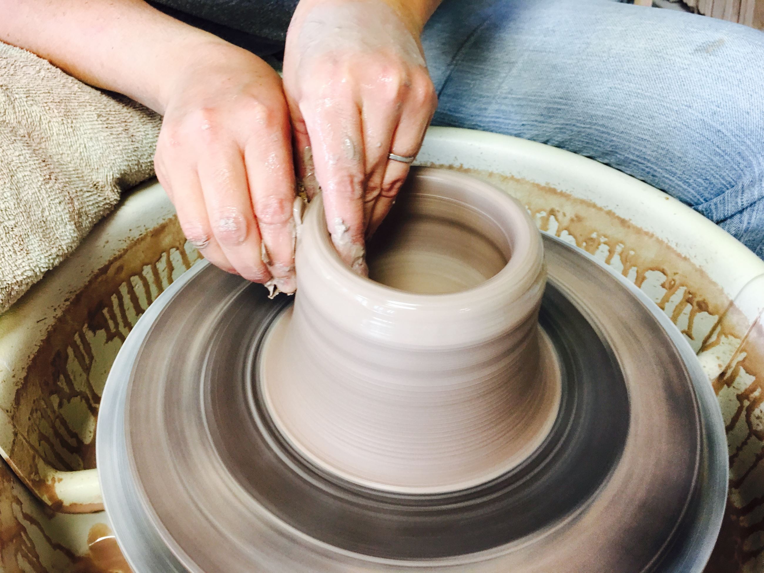 Hands building clay on a pottery wheel