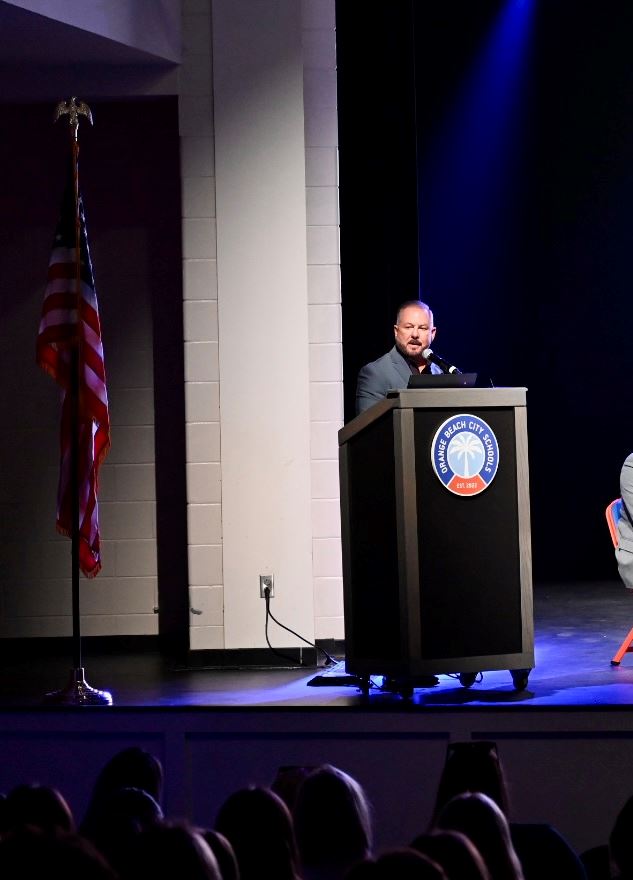 Man at podium on stage of the Orange Beach Performing Arts Center