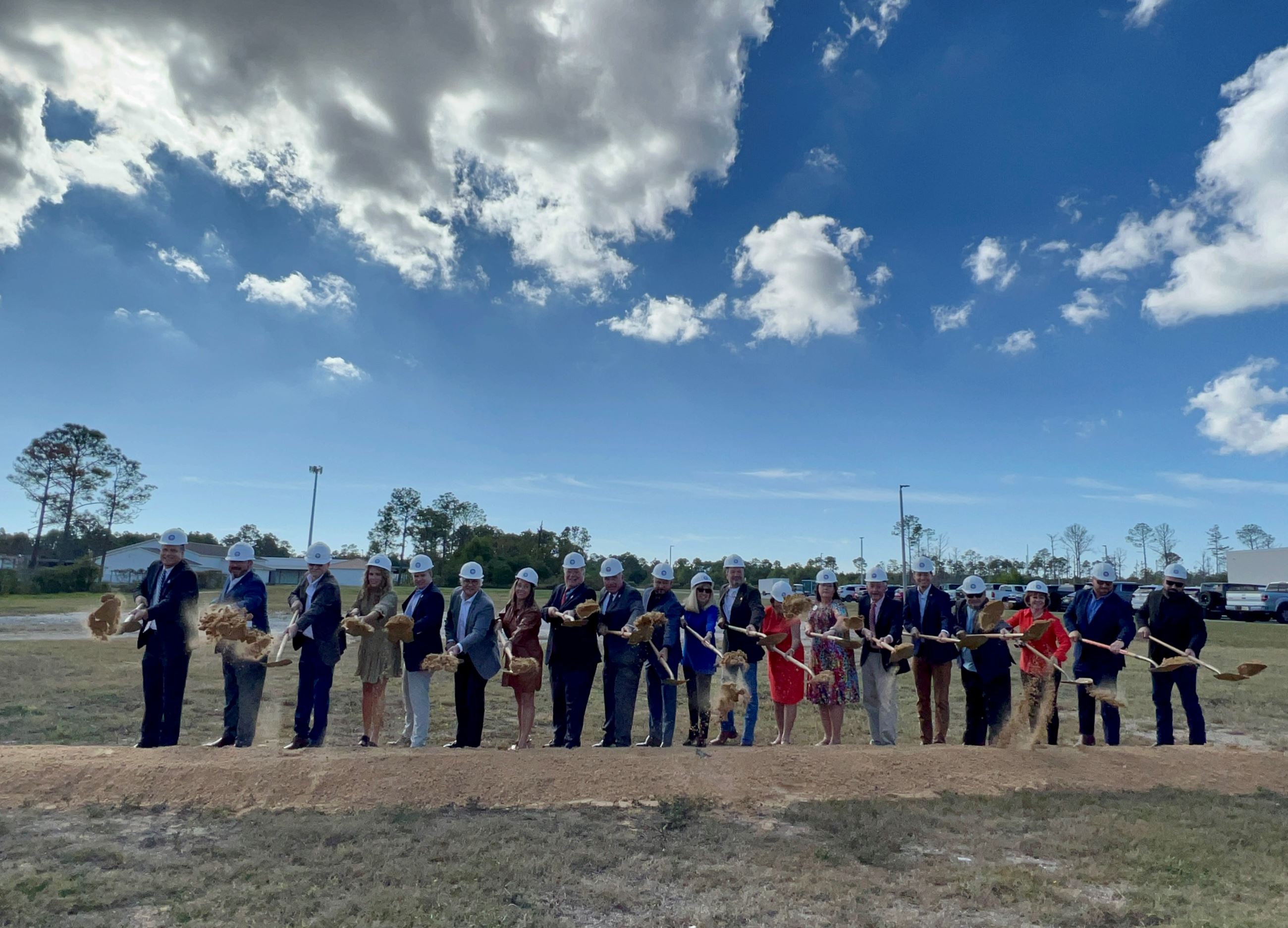 Officials throw dirt with gold shovels under partly cloudy skies